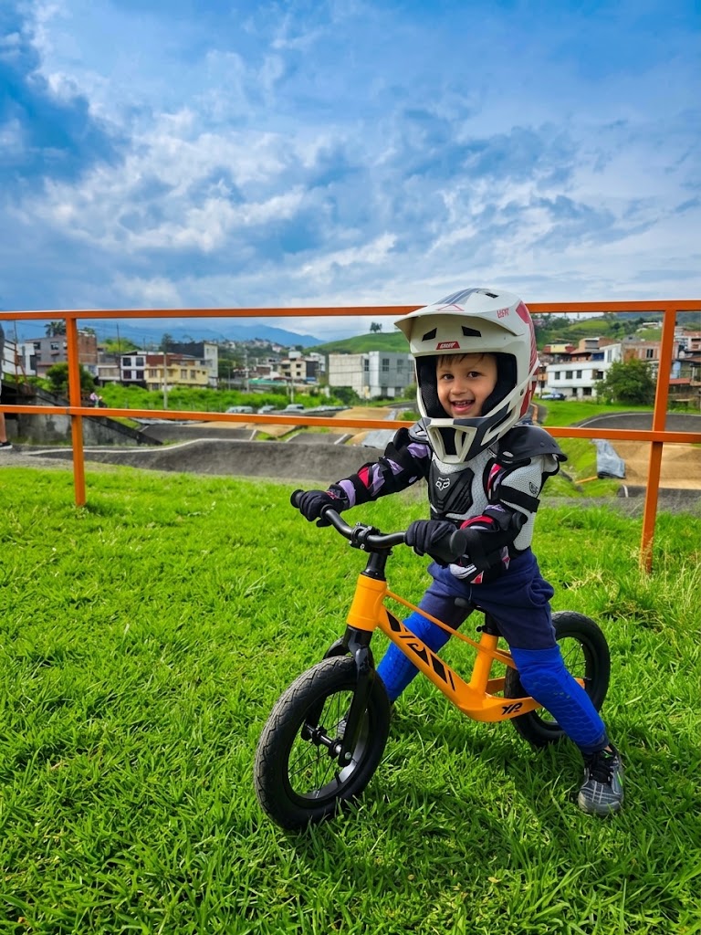 Niño sonriendo con casco sobre la bicicleta de balance YP Racing naranja en una pista de BMX