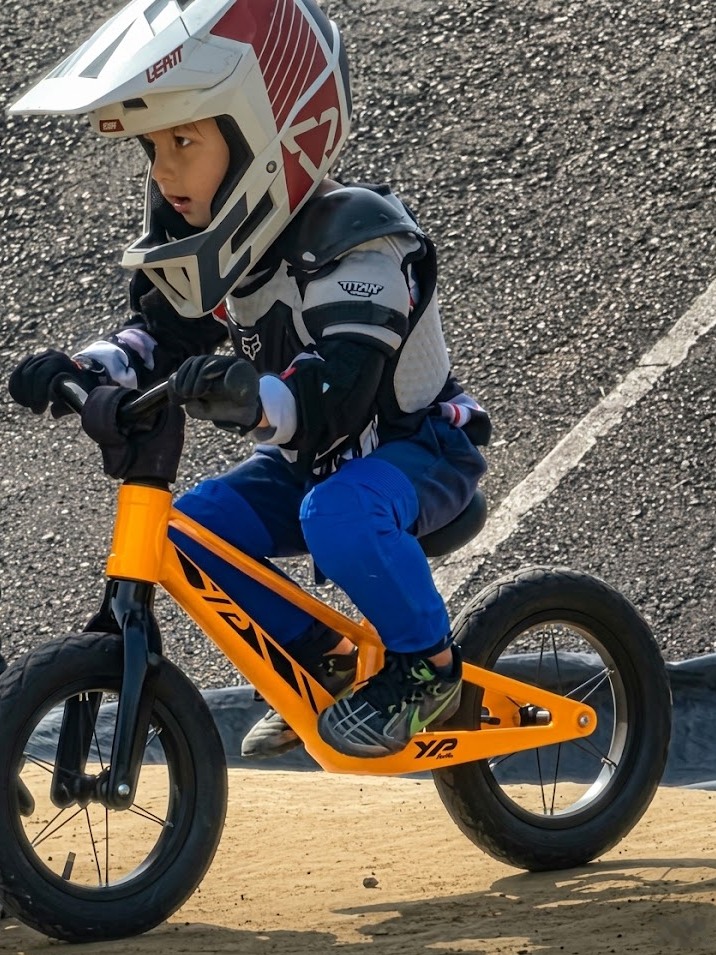 Niño con casco rodando con los pies arriba en la bicicleta de balance YP Racing naranja